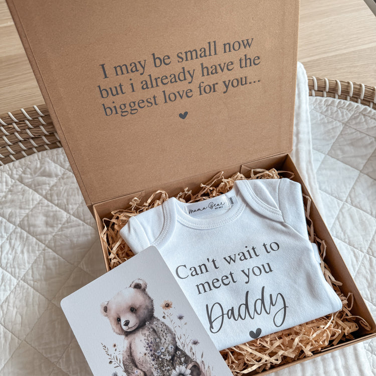 Baby announcement idea for boyfriend / partner. Brown kraft box, inside the lid it says in black serif font ' I may be small now but i already have the biggest love for you...' then inside the box is a white onesie that says 'Can't wait to meet you Daddy'. Pictured next to the onesie, is a little post card with a teddy bear illistration on it.