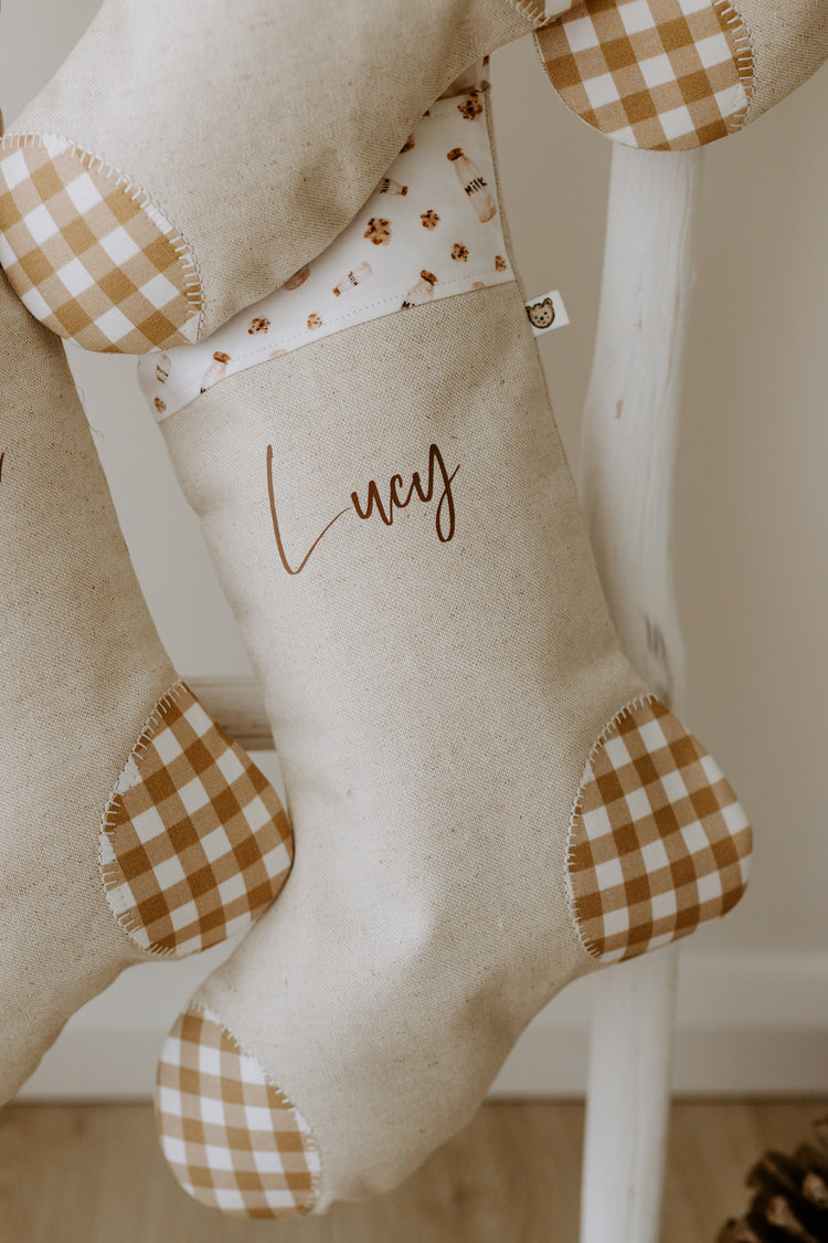 Milk and cookies Christmas stocking personalised with the name “Lucy.” Handmade linen stocking featuring a festive cuff with milk bottles and cookies print, plus mustard gingham heel and toe patches. Perfect personalised Christmas stocking for kids or adults, unique Australian handmade holiday décor.