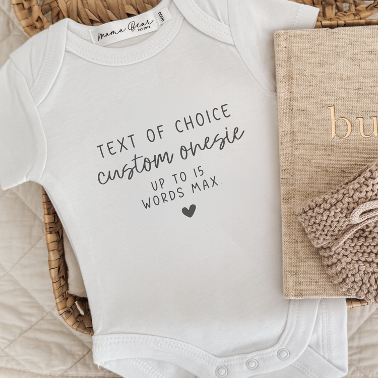 A white baby onesie with your own wording as the custom design. One says 'Text of choice custom onesie up to 15 words max' and a small solid heart.