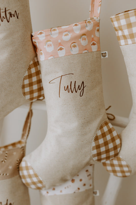 Neutral linen Christmas stocking personalised with the name Tully, featuring a pink Santa Claus cuff and tan gingham patchwork details.