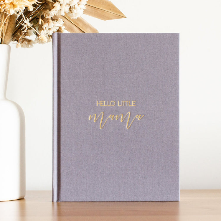 Photo of a pregnancy journal in a dark grey linen shade. The front of the book as gold writing on the front that says 'Hello Little Mama'.
