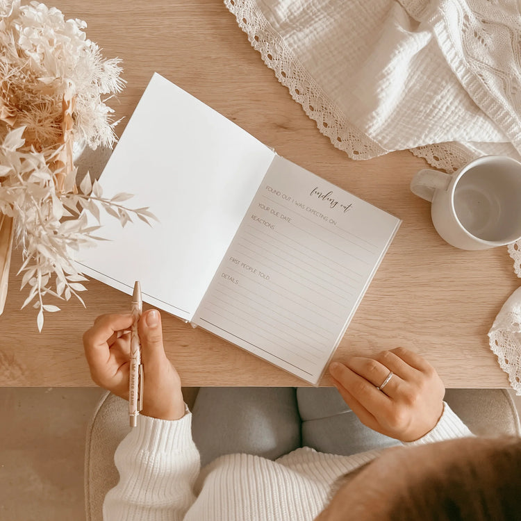 Photo of a pregnant Mummy to be, writing in a pregnancy journal. This page has written prompts such as... 'Finding out. Found out i was expecting on...' 'Due date' 'first people told' and 'details'.