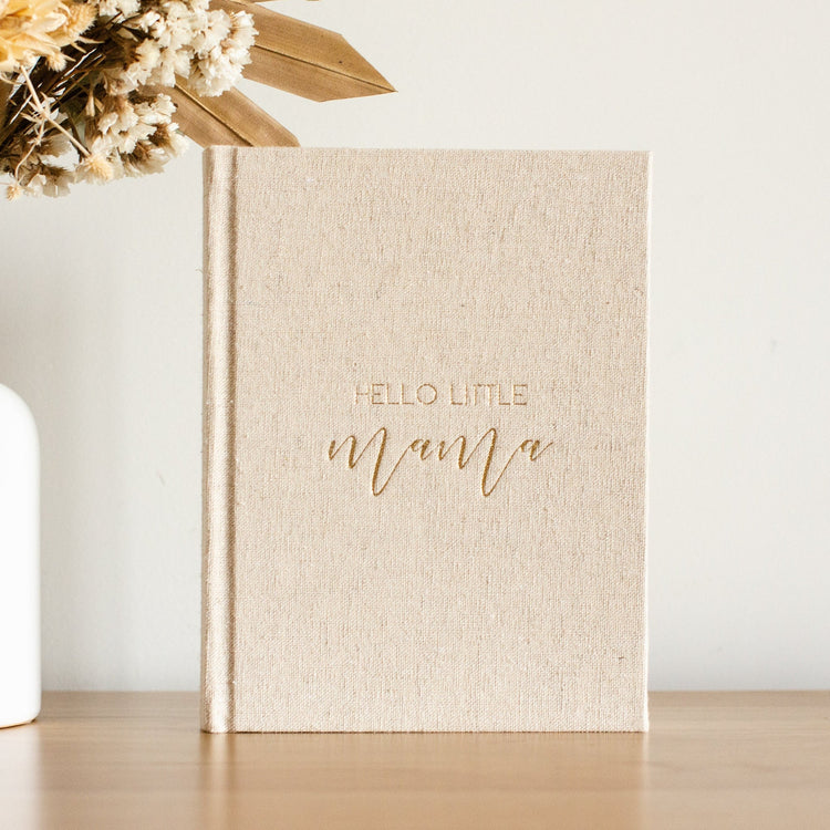 A Photo of a sand linen journal with gold writing on the front saying 'Hello Little Mama'. This journal is for the Mother to be to write in about her pregnancy journey.