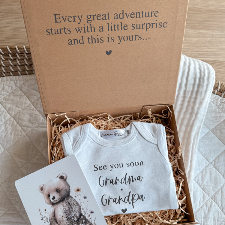 Baby announcement to parents aka Grandparents to be. Kraft brown magnetic close box with black text on the top of box saying "Every great adventure starts with a little surprise and this is yours..." Inside the raffia filled box is a white onesie with the text "see you soon Grandma & Grandpa".