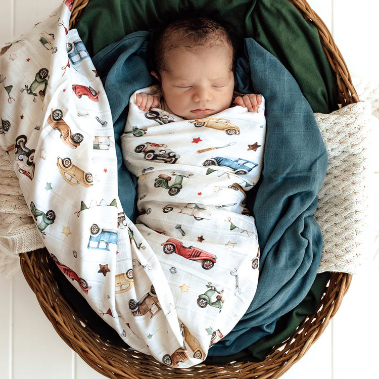 Newborn baby wrapped in a blanket with car patterns in a wicker basket.