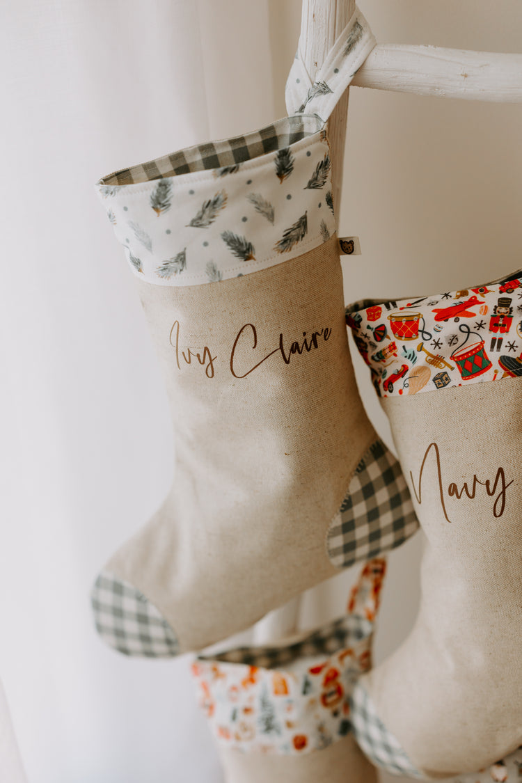 Gift idea, Handmade personalised Christmas stocking in beige fabric with green gingham heel and toe, featuring a pine branch print cuff, customised with name Ivy Claire.