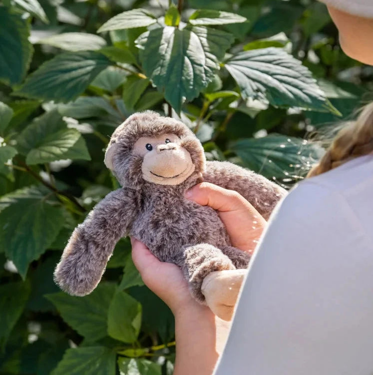 Person holding a monkey plush toy in front of green foliage
