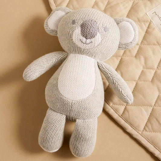 Knitted light grey koala bear on a beige quilted surface