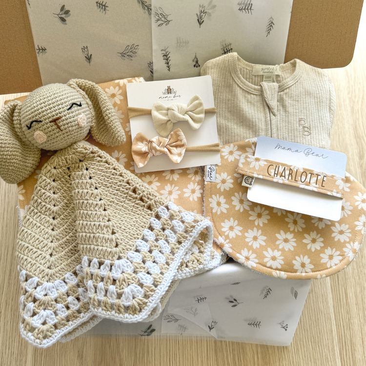 Baby girl gift idea - Kraft box filled with neutral beige and caramel Daisy hues. A crochet bunny light brown comforter, a bib, hairbow, burp cloth & personalised dummy clip in a honey caramel Daisy fabric. Tied in with a light beige ribbed zipsuit.