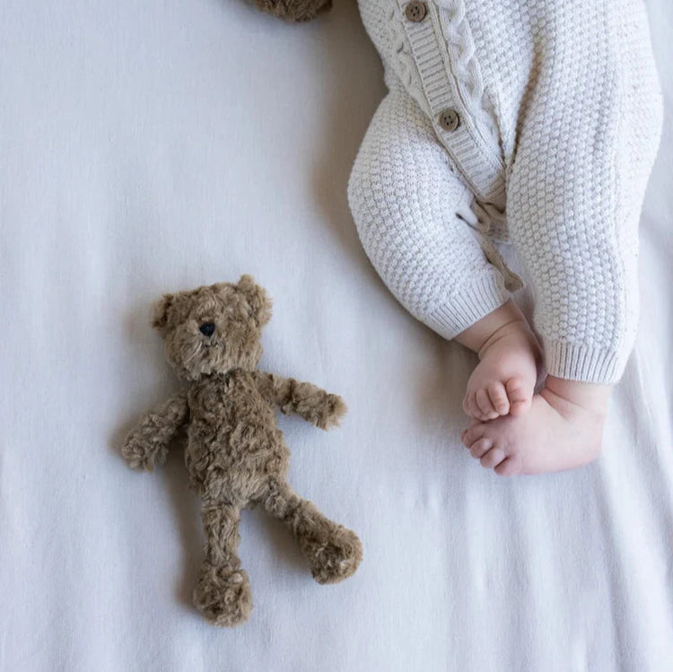 A baby lying next to a brown teddy bear rattle on a light background.