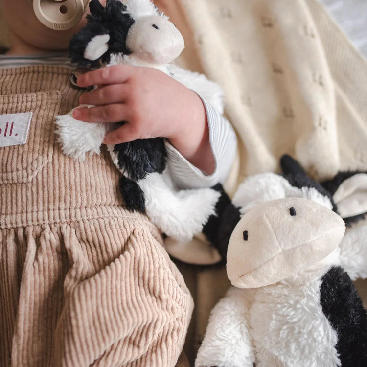 Baby holding a black and white farm cow toy. A bigger version of this toy lays beside him.