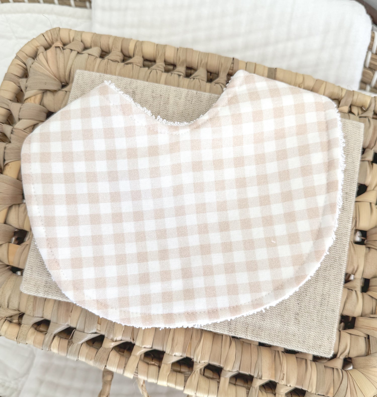 Handmade baby bib with a soft beige and white gingham check pattern, contoured for newborn comfort and a lovely gender-neutral gift option.