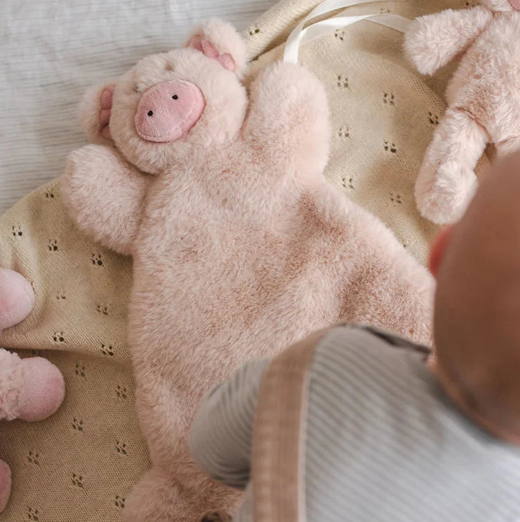 Photo inside a cot with a flatlay of a pink plush pig toy baby comforter.