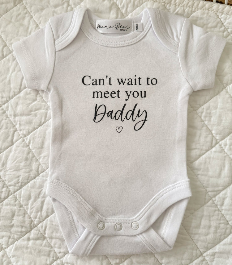 White baby onesie with 'Can't wait to meet you Daddy' text on a quilted surface