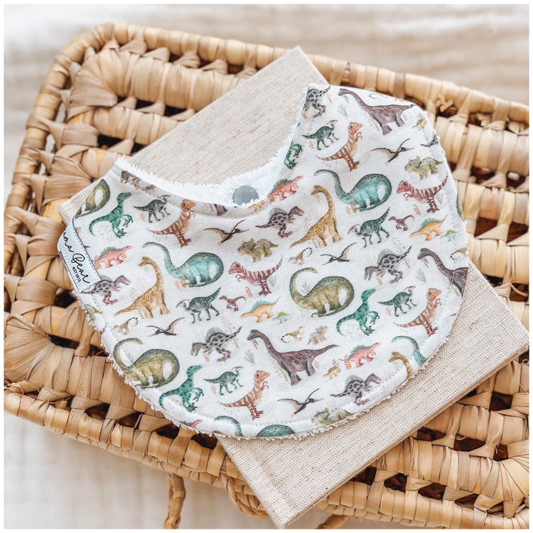 baby bib featuring an all-over dinosaur print in muted greens, browns, and rust tones. Handmade and perfect for babies or toddlers who love dinosaurs.