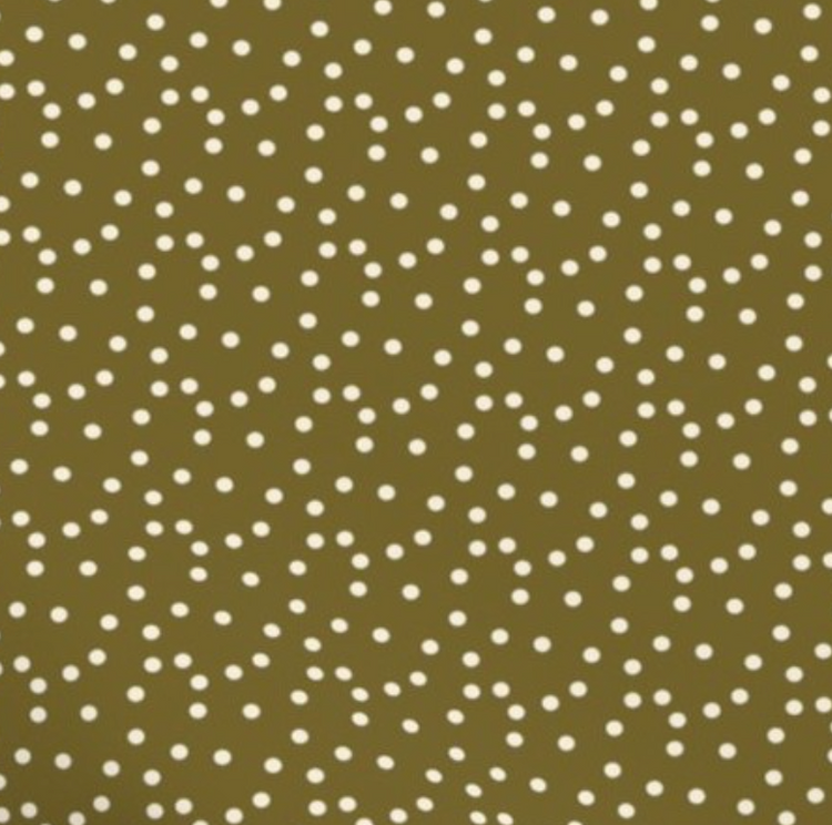 Sage green baby bib with a white polka dot print, styled on a woven basket with a neutral cloth underneath.
