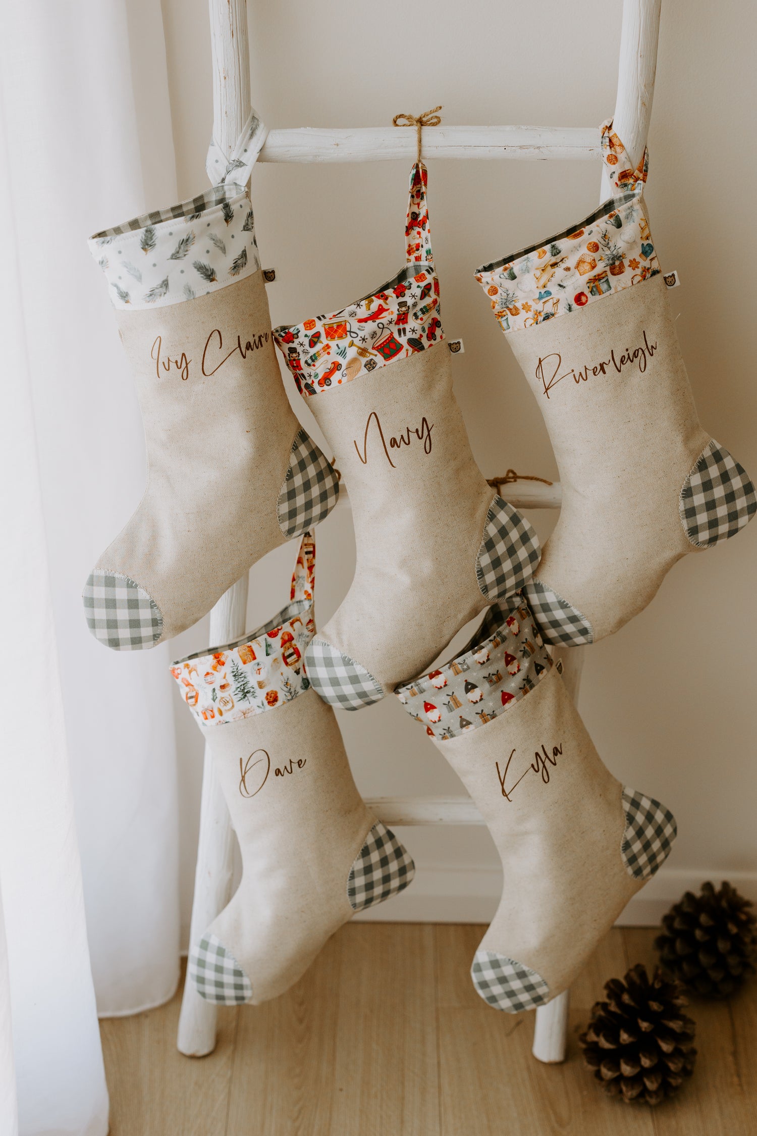 Set of handmade personalised Christmas stockings in beige fabric with green gingham detail and assorted festive cuffs, customised with names Ivy Claire, Navy, Riverleigh, Dave and Kyla.