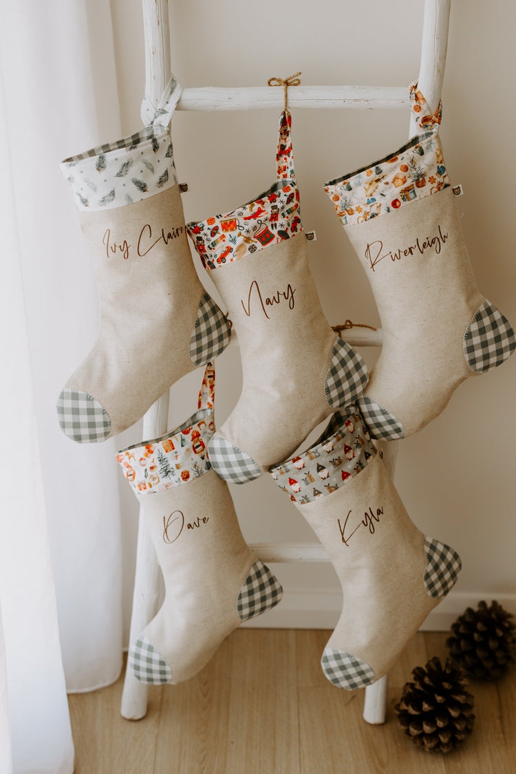 Set of handmade personalised Christmas stockings in beige fabric with green gingham detail and assorted festive cuffs, customised with names Ivy Claire, Navy, Riverleigh, Dave and Kyla.