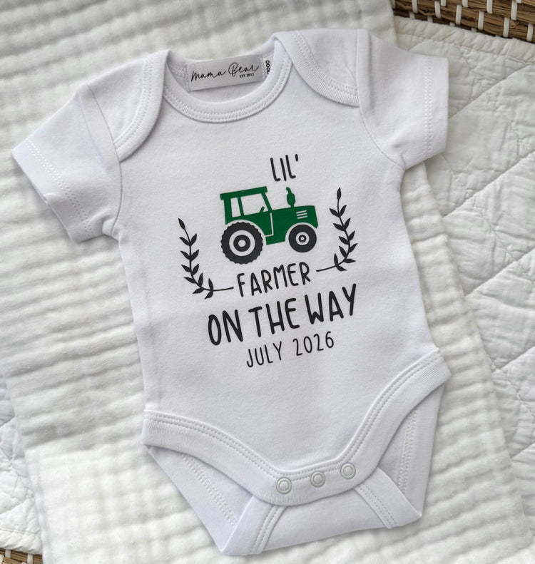 White baby onesie with 'Lil' Farmer On The Way' design on a textured surface