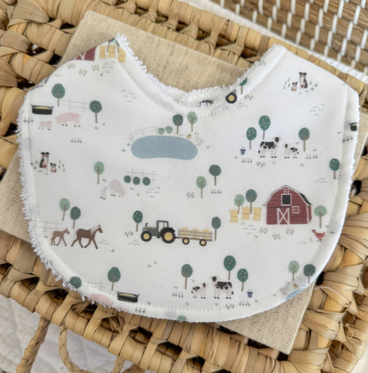 Baby bib with farm-themed pattern on a woven surface
