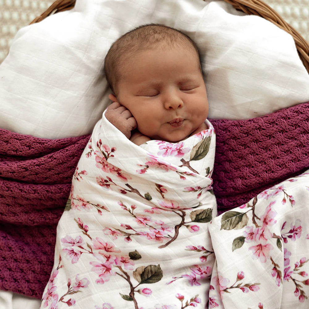 Newborn baby wrapped in a floral cherry blossom blanket swaddle.