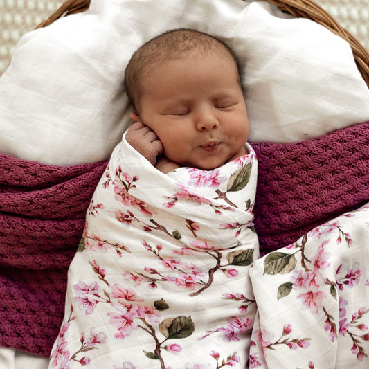 Newborn baby wrapped in a floral cherry blossom blanket swaddle.