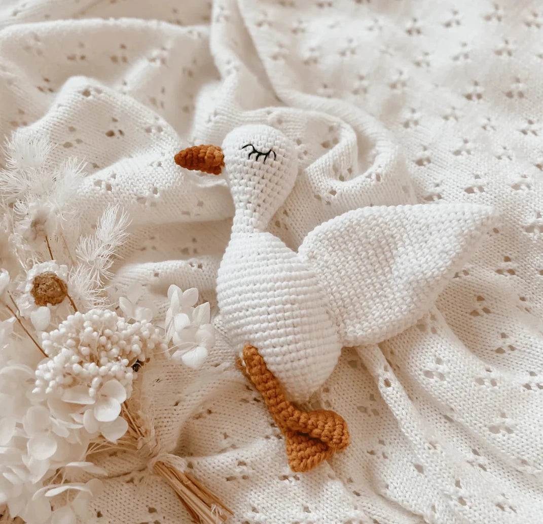 Knitted goose toy on a textured white fabric background with flowers.