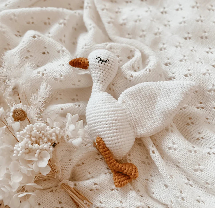 Knitted goose toy on a textured white fabric background with flowers.