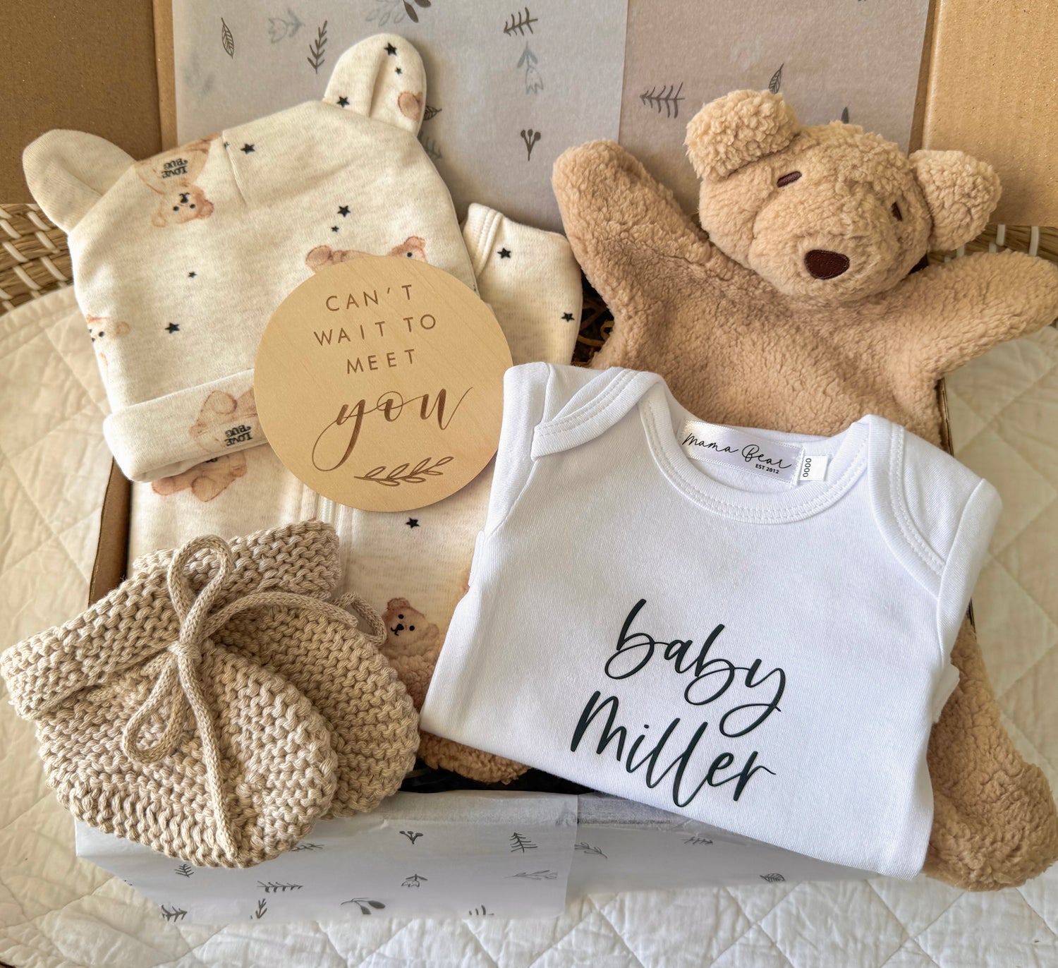 Gender-neutral baby announcement gift hamper featuring a soft beige teddy bear, personalised baby announcement onesie, wooden milestone disc, and coordinating baby essentials, all beautifully arranged in a gift box with neutral tones and natural textures, perfect for baby showers or special announcements. 