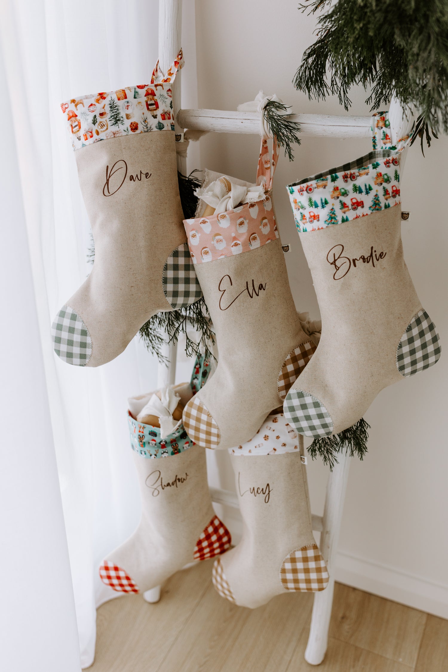 Set of handmade personalised Christmas stockings with festive fabric cuffs including Santa print, farm tractor print, dog print, and milk & cookies print, each with custom names in script font.