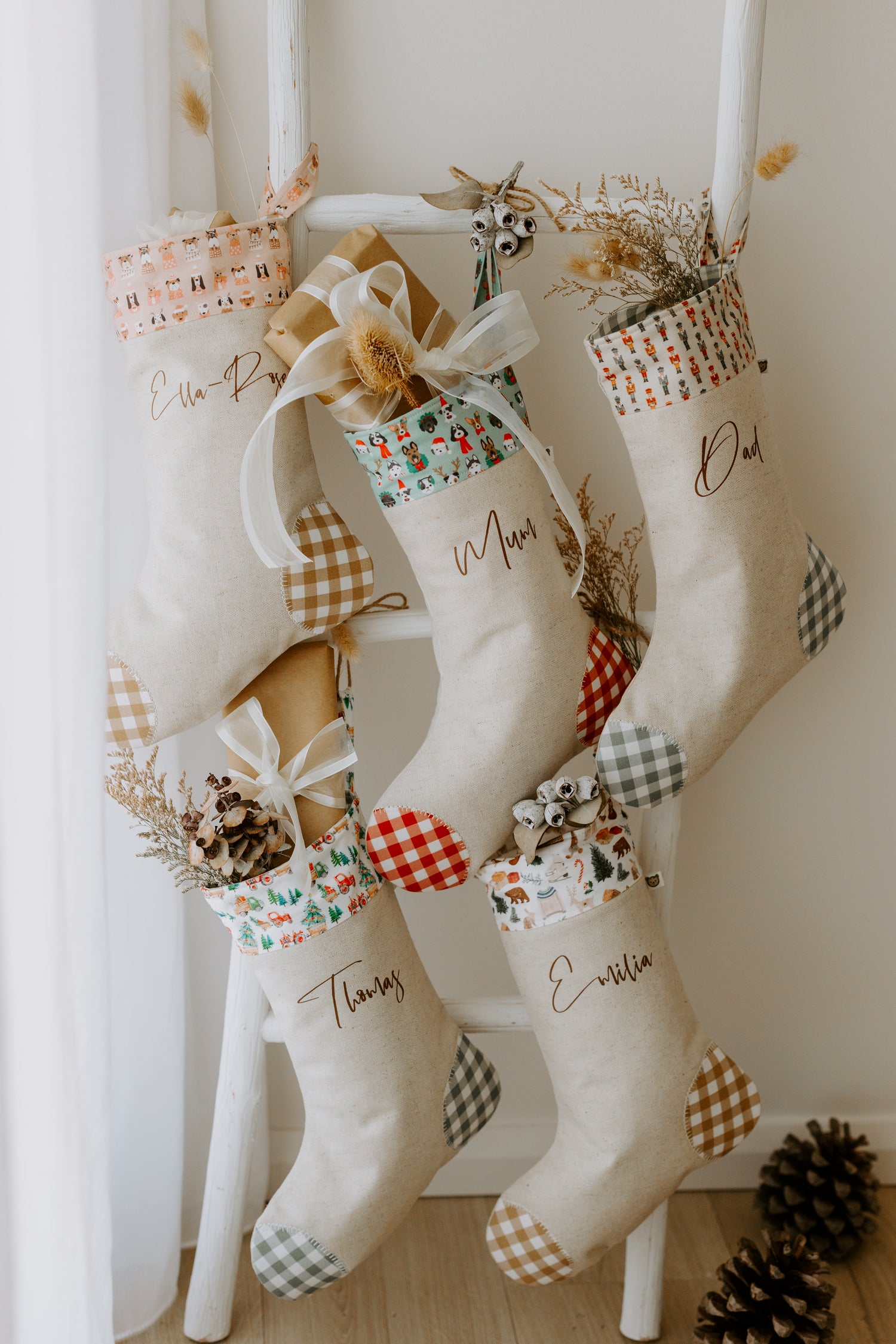 Set of handmade personalised Christmas stockings for the whole family & pets in beige fabric with gingham detail and assorted festive cuffs including pink puppy dog print, nutcracker print, woodland animals and classic Christmas motifs, customised with names Ella-Rose , Mum, Dad, Thomas and Emilia.