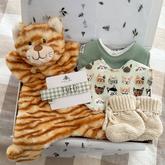 Baby gift box featuring a soft plush ginger cat comforter, a sage gingham dummy clip personalised with babies name, a solid sage baby bib and a coordinating bib with cute cat face illustrations. Lastly a knit pair of honey beige booties inside a white gift box.