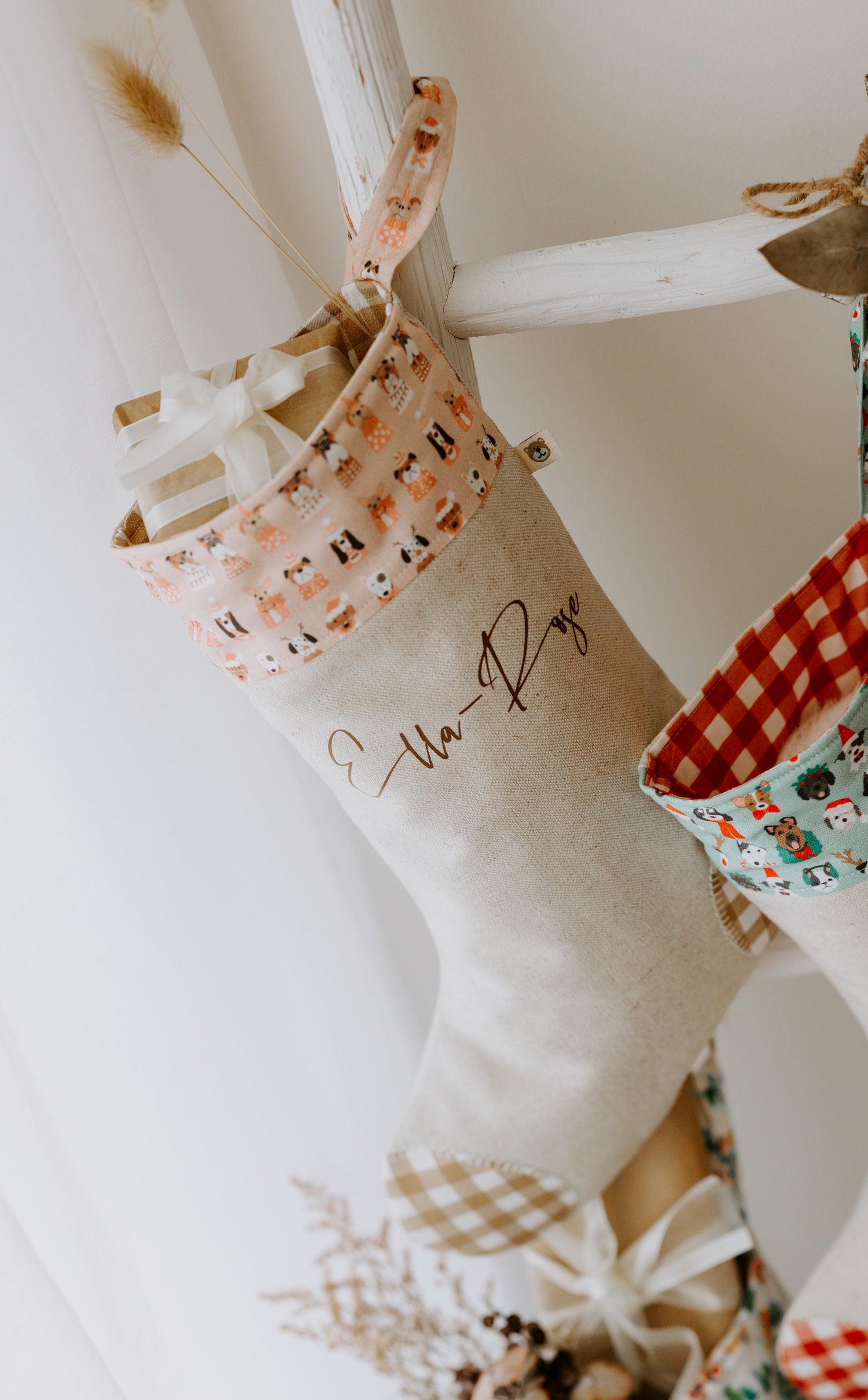 Handmade personalised girls Christmas stocking in beige fabric with caramel gingham trim and pink cuff featuring festive puppy dog print, customised with name Ella-Raye.