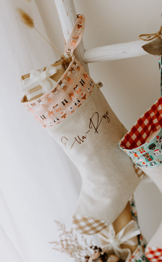 Handmade personalised girls Christmas stocking in beige fabric with caramel gingham trim and pink cuff featuring festive puppy dog print, customised with name Ella-Raye.