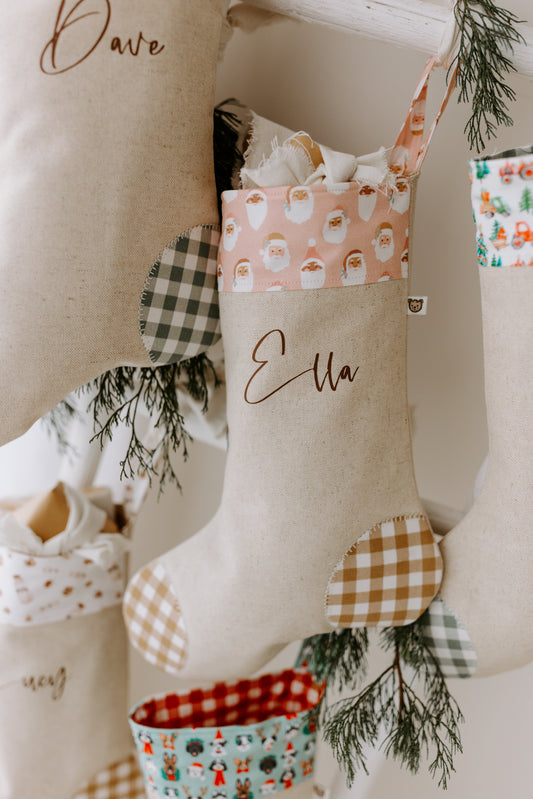 Handmade linen Christmas stocking with soft beige base, pink Santa print cuff, tan gingham patches, and personalised name Ella in script font.