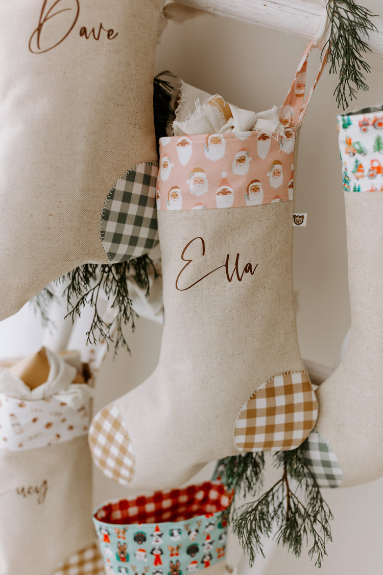 Handmade linen Christmas stocking with soft beige base, pink Santa print cuff, tan gingham patches, and personalised name Ella in script font.