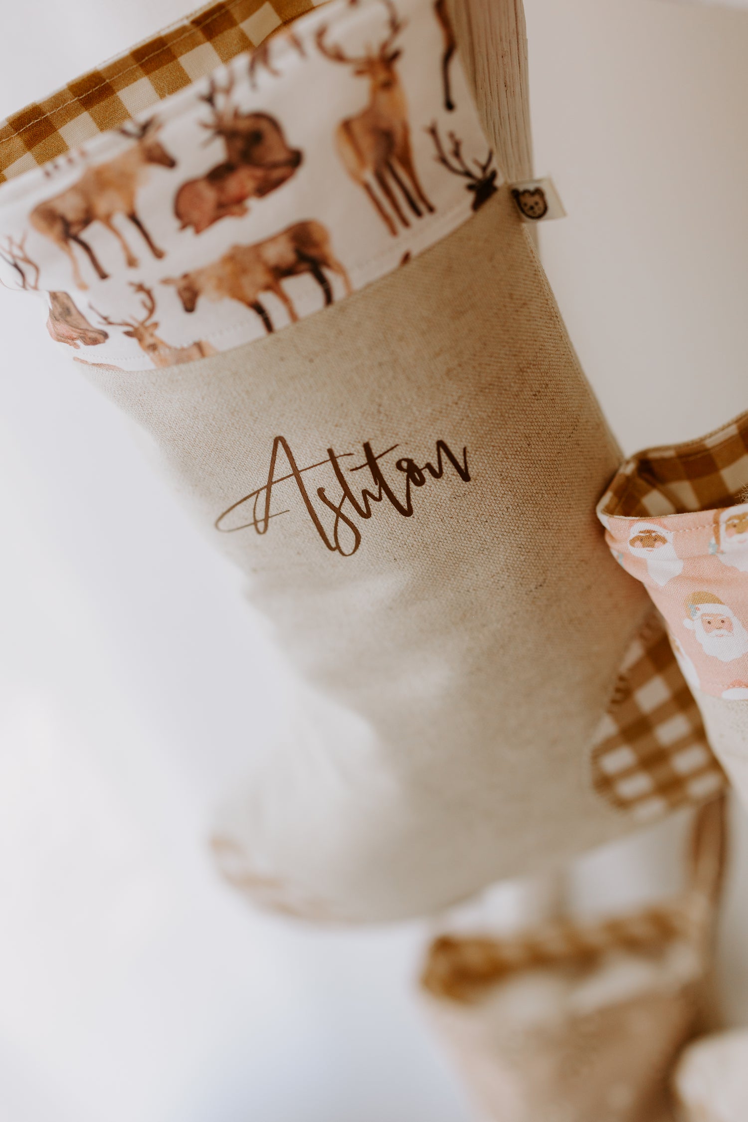 Handmade linen Christmas stocking personalised with the name “Ashton” in elegant script. The cuff is trimmed with a festive fabric showcasing detailed reindeer illustrations in various poses, adding a woodland charm. Natural beige tones and rustic design make it an ideal keepsake stocking for children or nature-inspired Christmas décor.