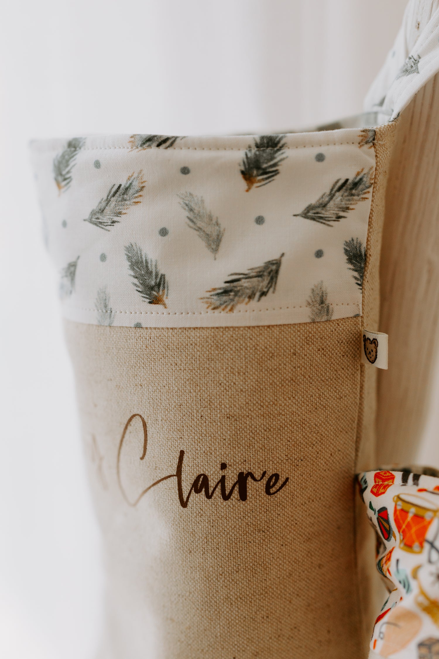 Baby first Christmas stocking with soft green leaves, personalised with name. The stocking is made of a beige linen type fabric, with the Ivy Claire written in brown script font the trim of the stocking is white with illustrations of green pine leaves. 