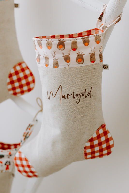Close-up of handmade personalised Christmas stocking in beige fabric with red gingham trim and reindeer print cuff, customised with name Marigold.