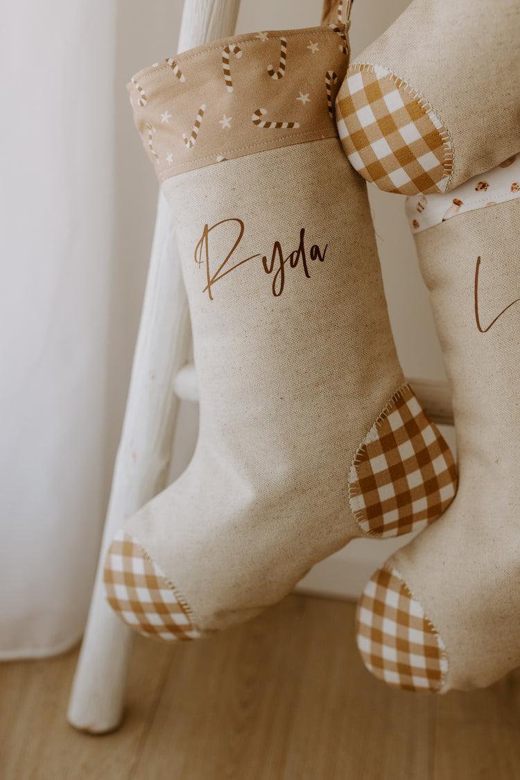 Personalised Christmas stocking handmade in beige fabric with caramel gingham heel and toe, featuring a candy cane print cuff, customised with name Ryda.