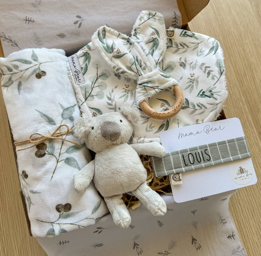 Gender neutral baby shower gift set featuring a personalised dummy clip, mini koala rattle, handmade bib, teething ring, and sage green leaf muslin swaddle. Packaged in a gift box with a card, ready for gifting.