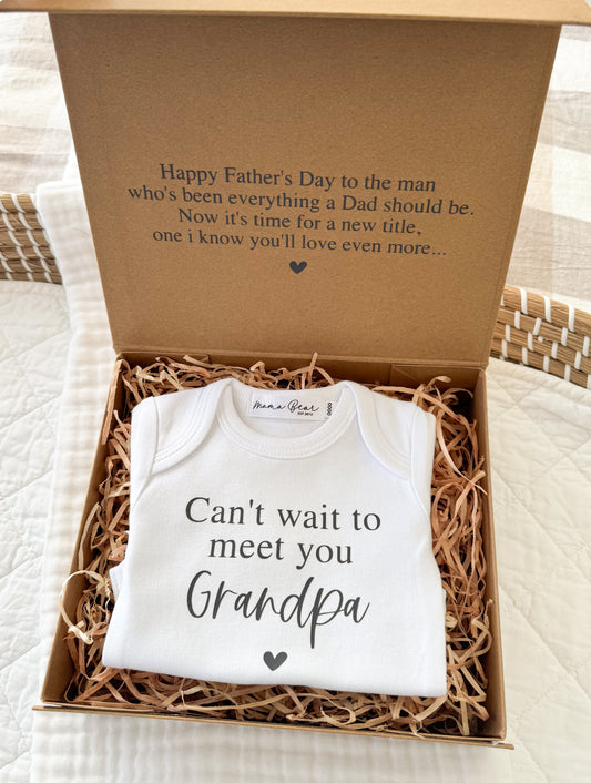 Raffia filled kraft brown giftbox. There is black text on top of the lid of giftbox which reads: "Happy Father's Day to the Man who's been everything a Dad should be.
Now its time for a new title, one i know you'll love even more..." then inside the box is a white onesie that reads " Can't wait to meet you Grandpa"