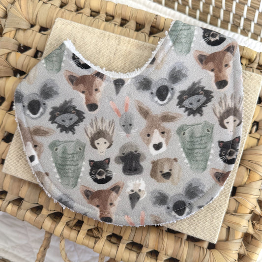 baby bib with Australian animal face illustrations on a grey background. Some animals include Kangaroo, koala, crocodile, emu.
