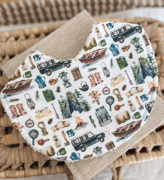 Handmade baby bib with an illustrated camping and adventure print featuring tents, lanterns, boots, 4WDs, canoes, and campfires; backed with absorbent terry towelling, ideal for messes and teething.