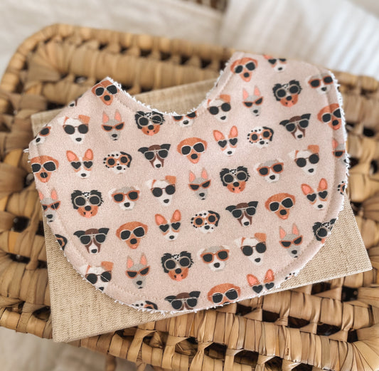 Blush / beige  baby bib with cartoon puppies wearing sunglasses in various breeds and styles; handmade in Australia with absorbent terry towelling backing for dribble and teething.