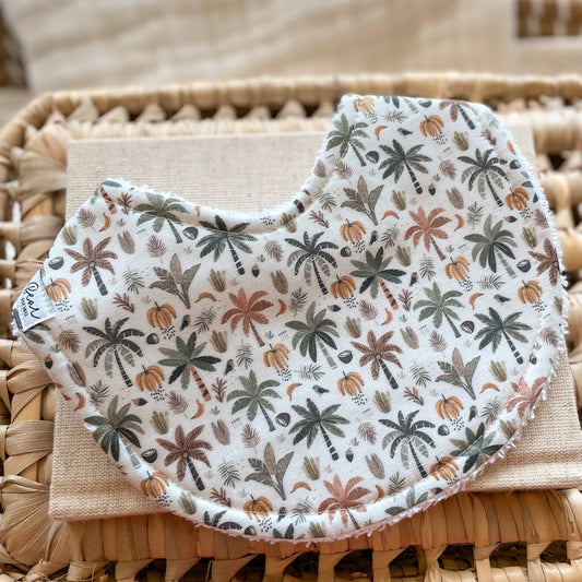Handmade baby bib with a tropical banana and palm tree print in muted earthy tones, backed with absorbent terry towelling—ideal for dribble, teething, and newborn gifts.