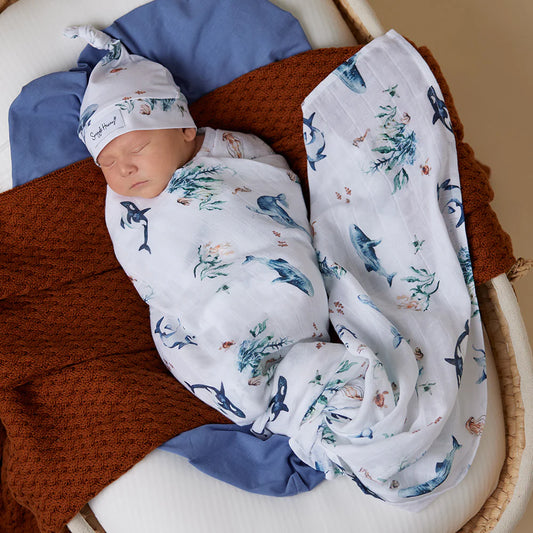Newborn baby boy wrapped in a white swaddle with illustrations of blue whales, sealife, seahorse, turtle, jelly fish etc.
