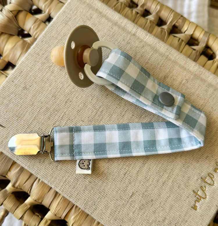 A baby dummy clip with a light blue and white gingham fabric strap.