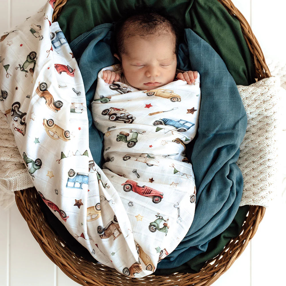 Newborn baby wrapped in a blanket with car patterns in a wicker basket.