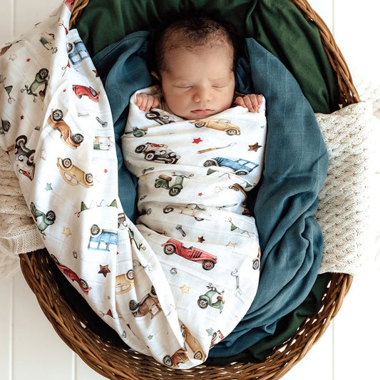 Newborn baby wrapped in a blanket with car patterns in a wicker basket.